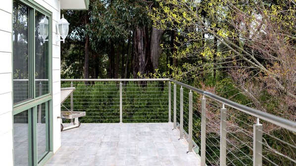 A balcony with a metal railing, a bench, and a view of trees and foliage.