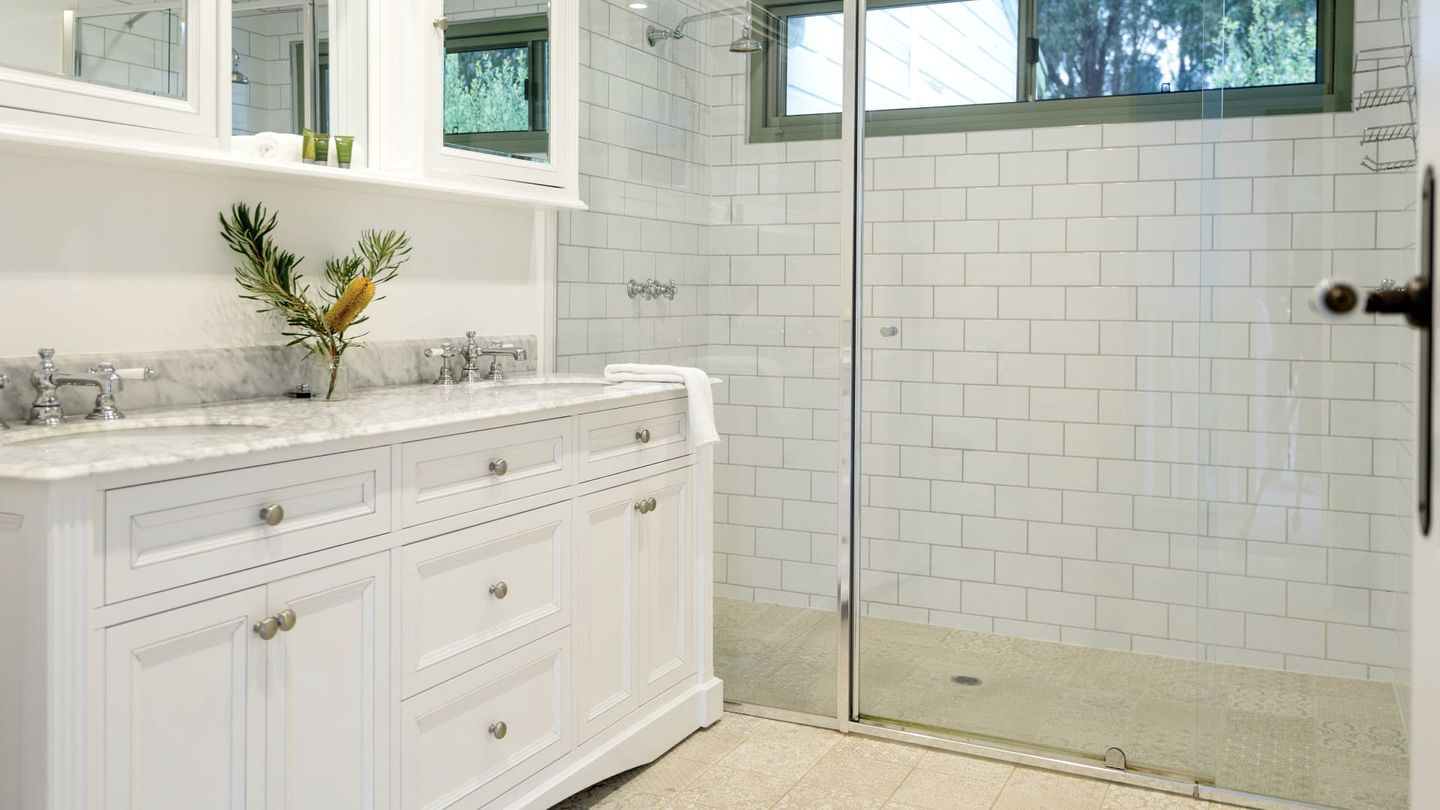 A bathroom with a white vanity, a glass shower enclosure, and a window with a view of trees.