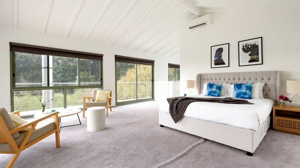 A bedroom with a large bed, a sofa, and a chair. There are three windows and a ceiling fan.