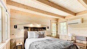 Une chambre dans une cabane en bois, avec un lit, une table de chevet, une lampe et un banc.
