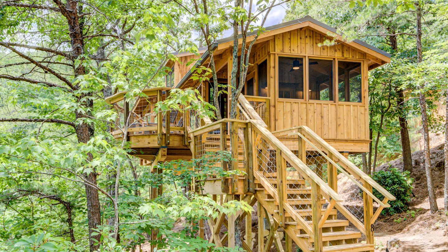 A wooden cabin with a staircase leading to a deck, surrounded by trees.