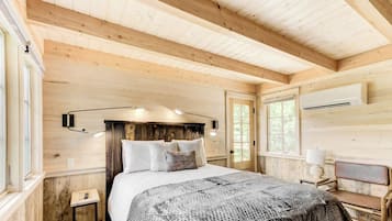 A wooden interior with a bed, bedside table, lamp, and window.
