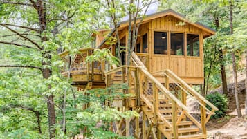 Eine Holzhütte mit einer Treppe, die zu einer Terrasse führt, umgeben von Bäumen.