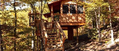 A wooden cabin with a staircase leading to a deck, surrounded by trees.
