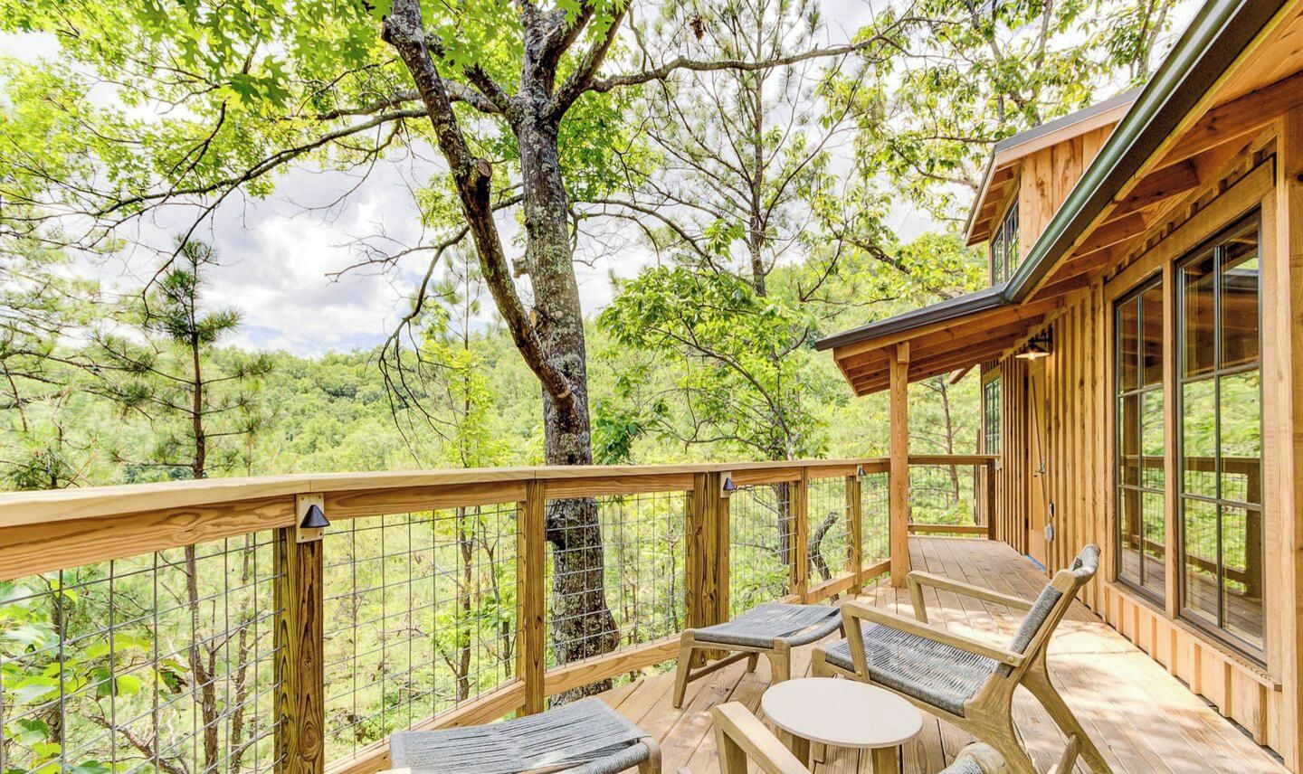 A wooden deck with a table and chairs, overlooking a forested area.