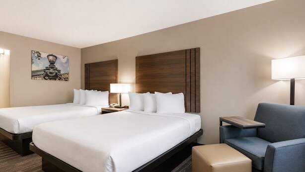 Ein Hotelzimmer mit zwei Betten, einem Schreibtisch, einem Stuhl und einem kleinen Hocker.