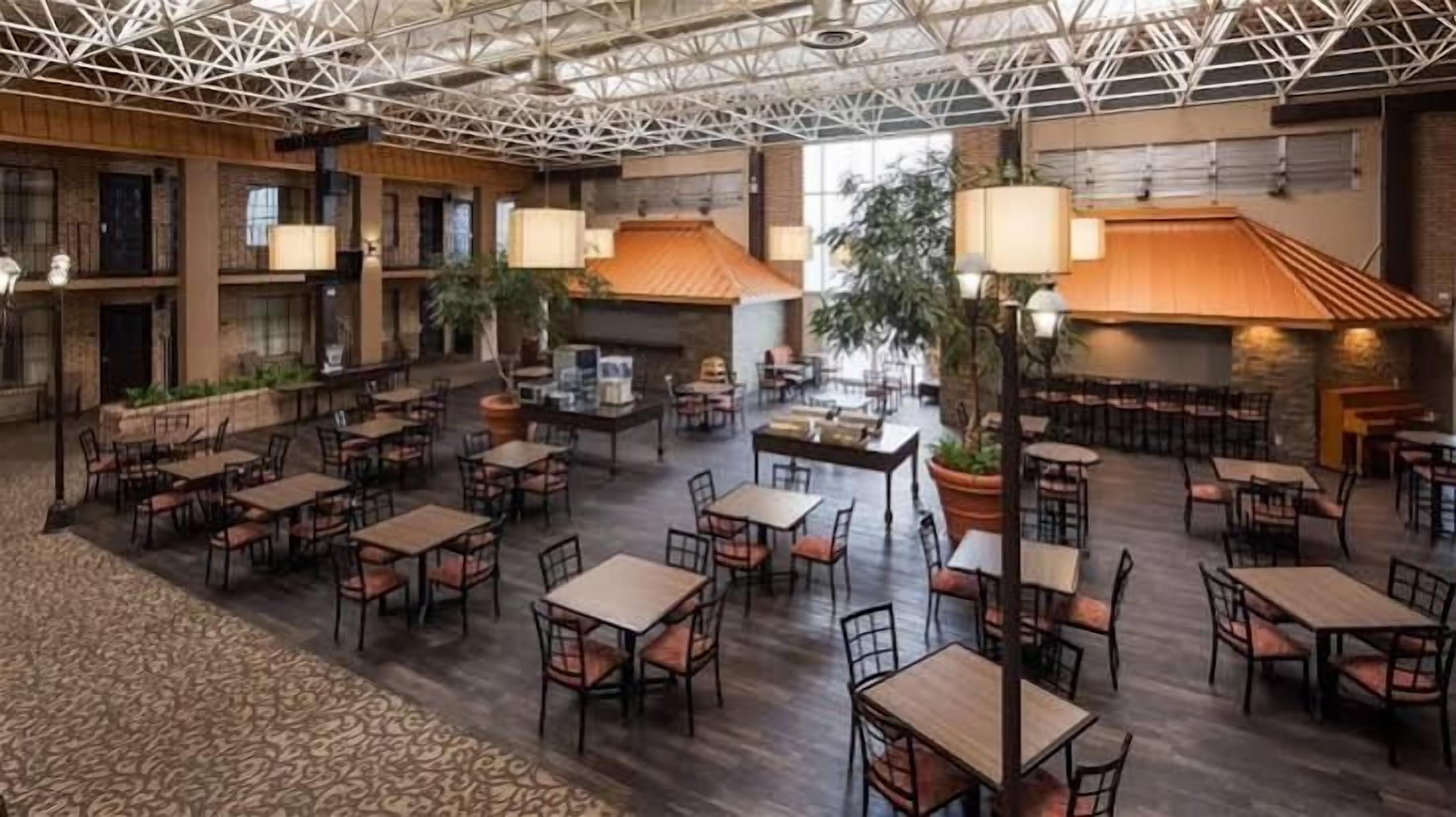 Un vaste espace intérieur aménagé en salle à manger, avec de nombreuses tables et chaises, un haut plafond doté d’une structure en treillis et une cheminée.