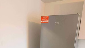 Un refrigerador de acero inoxidable en una cocina con un bote de basura y una mopa.