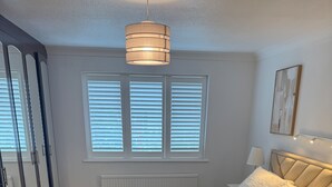 A bedroom with a bed, bedside tables, a mirror, and a window with blinds. - Apartment Sleeps 6 With Parking (Stanmore)