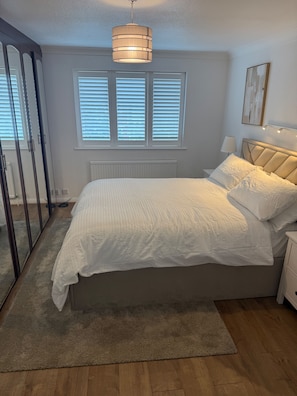 Un dormitorio con cama, mesitas de noche, un espejo y una ventana con persianas.