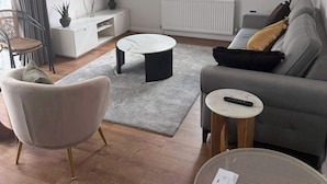 A modern living room with a flat-screen TV, a grey sofa, a round coffee table, a wicker chair, and a small side table. - Apartment Sleeps 6 With Parking (Stanmore)