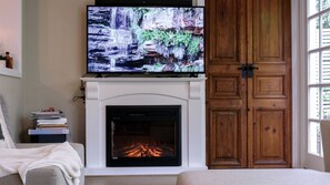 A living room with a fireplace, a television mounted above it, and a wooden cabinet to the right.