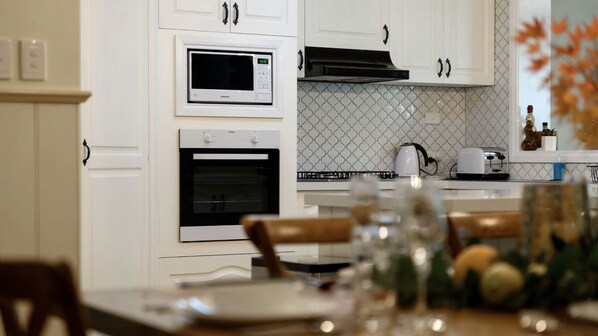 A modern kitchen with white cabinetry, a microwave, oven, and a kettle.