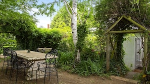An outdoor garden with a table and chairs, surrounded by lush greenery and a wooden pergola. - Cozy, Pet Friendly Cabin with Fireplace in Daylesford, Victoria (Daylesford)