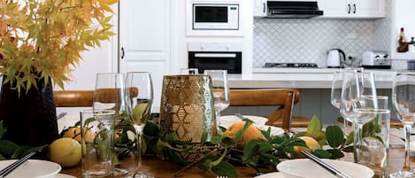 Une table à manger dressée avec des assiettes, des verres et des couverts, entourée de feuilles d’automne et agrémentée d’un vase décoratif.