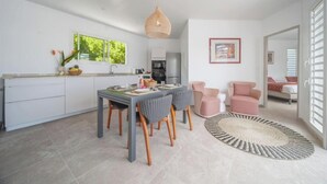 A modern kitchen with white cabinets, a dining area with a table and chairs, and a living room with a pink chair and a round rug. - Creole Villas (10 people)•Swimming Pools•Beach within walking distance (Sainte-Luce)