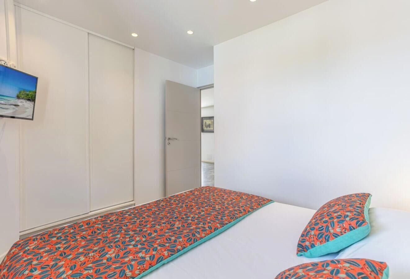 A single bed with a patterned bedspread and matching pillows, a white wardrobe, and a door leading to another room.