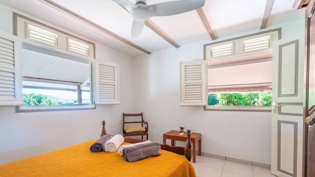 Ein Zimmer mit einem Bett, einem Sessel, einem kleinen Tisch und einem Fenster mit Rollläden.