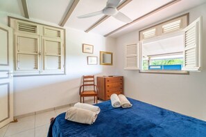 A bedroom with a bed, a chair, a dresser, and a ceiling fan. - Coffee Plantation House, Villa & Bungalow with Ocean View (Le Carbet)