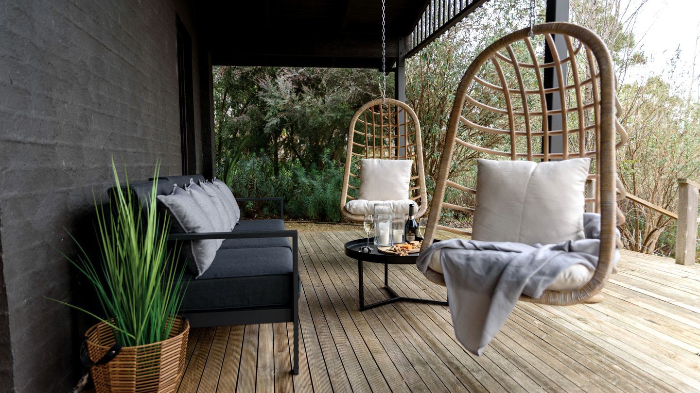 Una terraza de madera con un sofá, una hamaca colgante y una mesa con una botella y vasos.