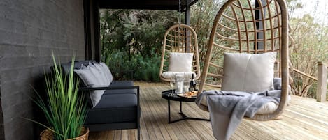 Una terraza de madera con un sofá, una hamaca colgante y una mesa con una botella y vasos.