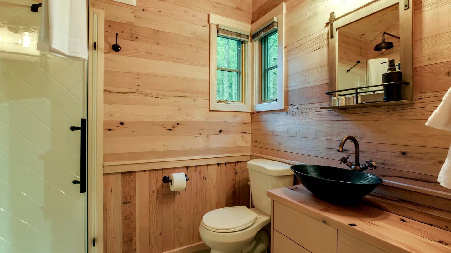 Een houten badkamer met toilet, wastafel en een raam.