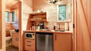 A compact kitchen with wooden cabinets, a stainless steel dishwasher, and a window above the sink.