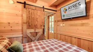 Interior de madera con una cama, una puerta corrediza estilo granero y un cartel de AYRES Vacation Rentals.
