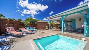 Ein Garten mit Swimmingpool, Liegestühlen, einer überdachten Terrasse und einem Holzzaun.