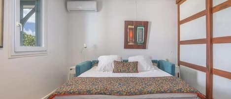 A bedroom with a bed, a window, an air conditioning unit, and a sliding door.