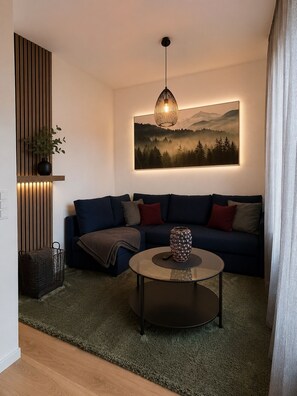 Una sala moderna con un sofá azul oscuro, una mesa de centro redonda y una lámpara colgante.