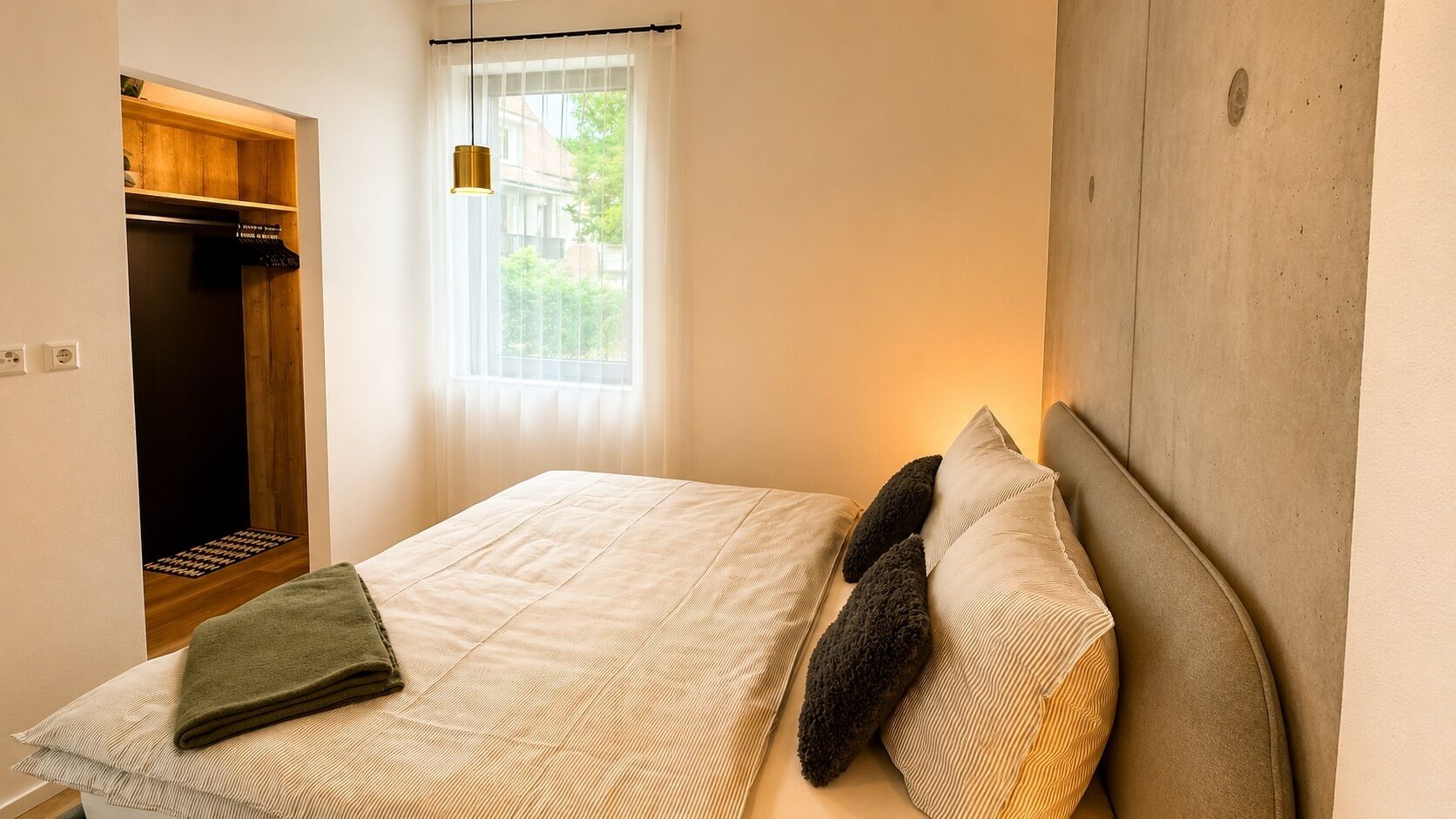 Ein Schlafzimmer mit Bett, Kleiderschrank, Fenster und einer Pendelleuchte.
