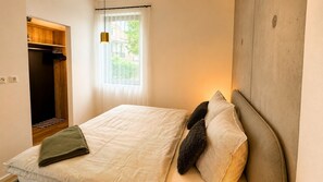 Un dormitorio con cama, armario, ventana y lámpara colgante.
