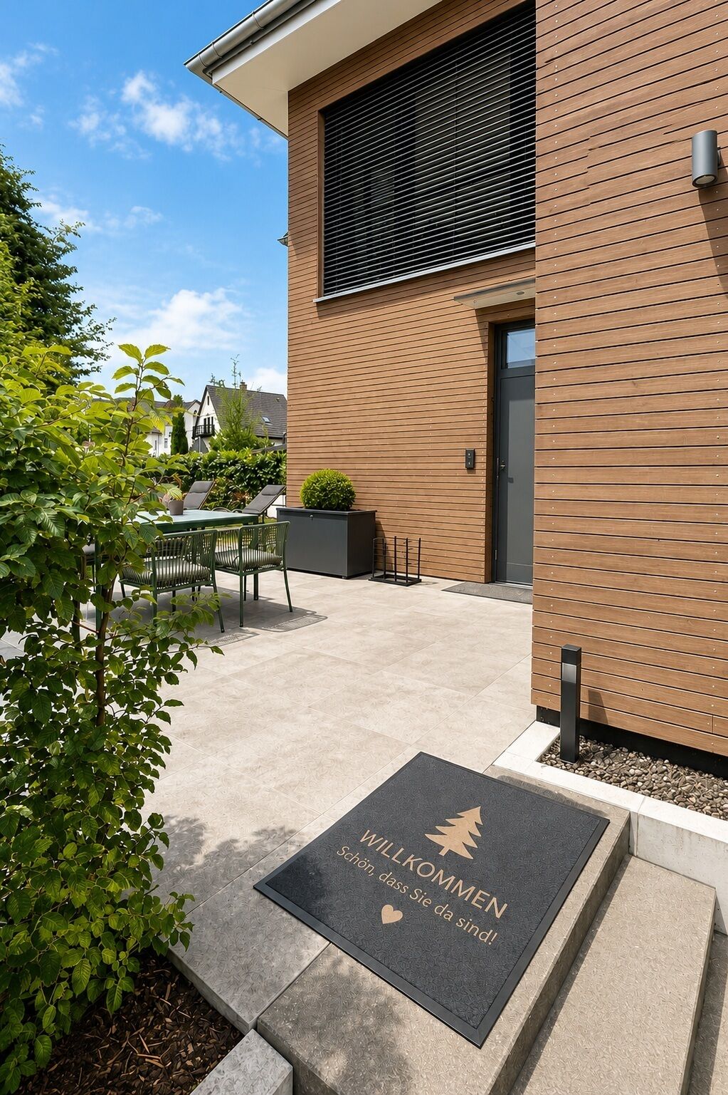 A modern building with a wooden facade, a black door, and a welcome mat with German text.