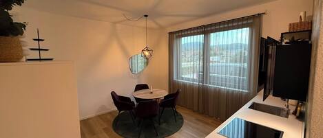 Ein kompakter Wohnraum mit Essbereich, einer kleinen Küche und einem großen Fenster mit Vorhängen.