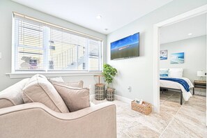 A modern bedroom with a bed, a TV, and a view of the sea through large windows. - Seaside Retreat: Salty Shore Getaway (Wildwood)
