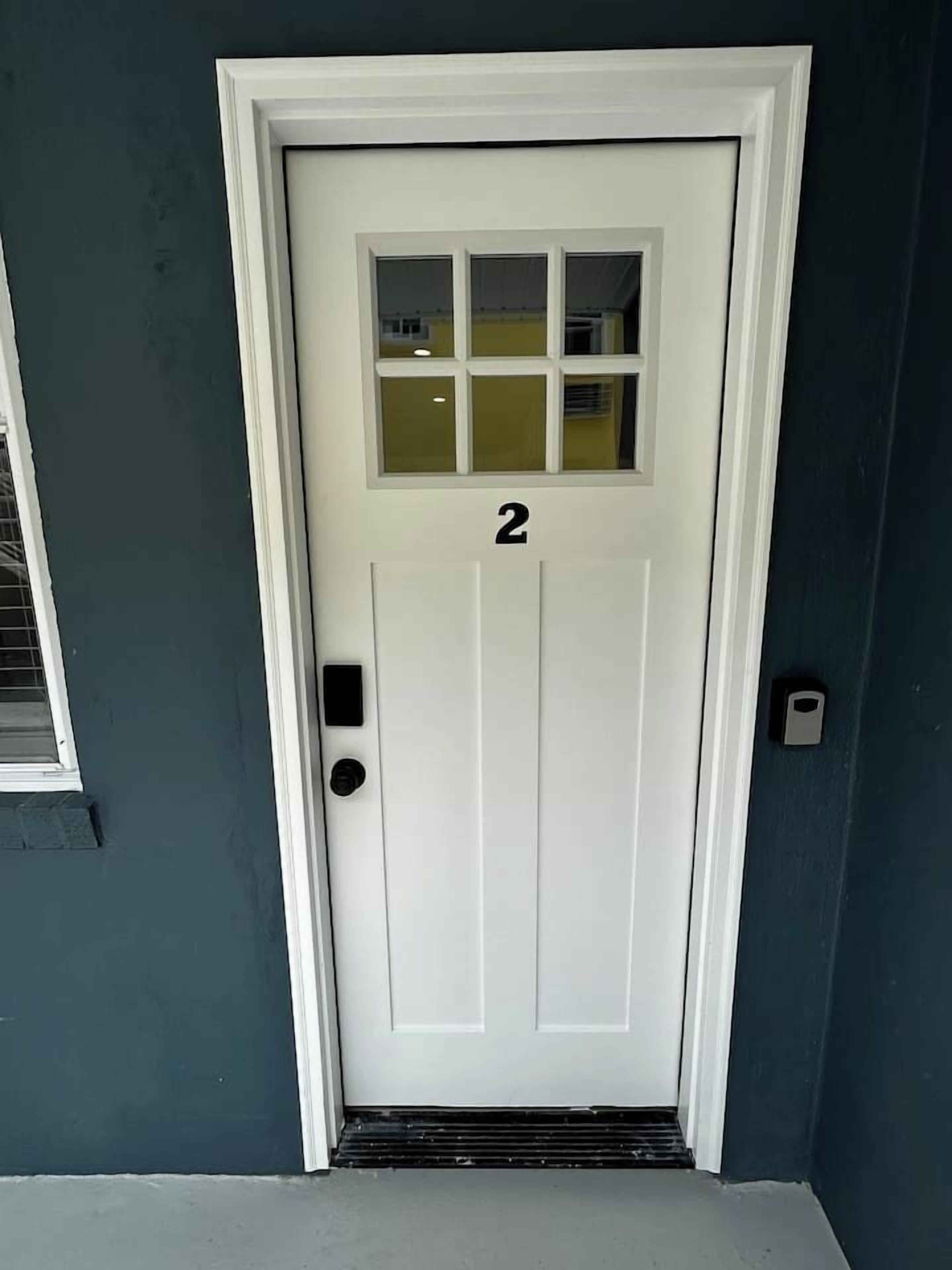 Uma porta branca com o número 2, uma pequena janela acima e um interfone do lado direito.