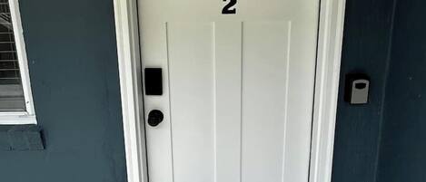 Une porte blanche avec le numéro « 2 » dessus, une petite fenêtre au-dessus de la porte et un interphone sur le côté droit.