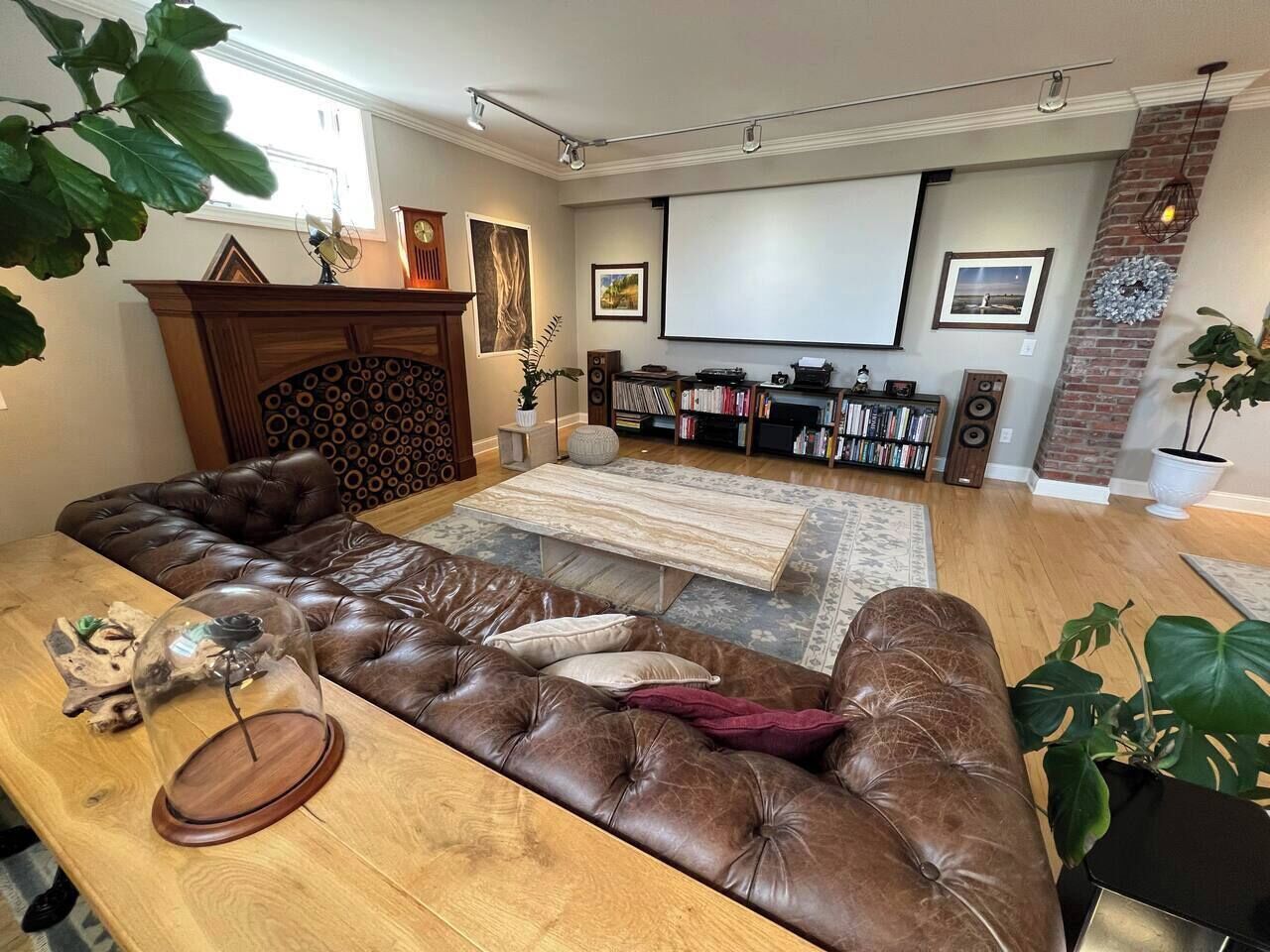 Una sala de estar con un sofá modular, una mesa de centro, una chimenea, una estantería y una pantalla de proyector.