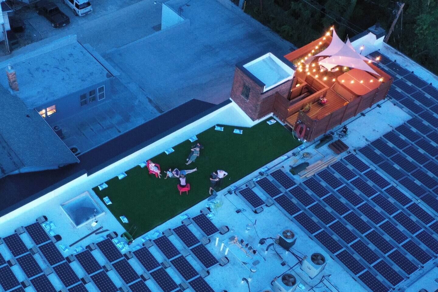 Un toit équipé de panneaux solaires, un petit espace vert avec des sièges et un bâtiment décoré de guirlandes lumineuses.