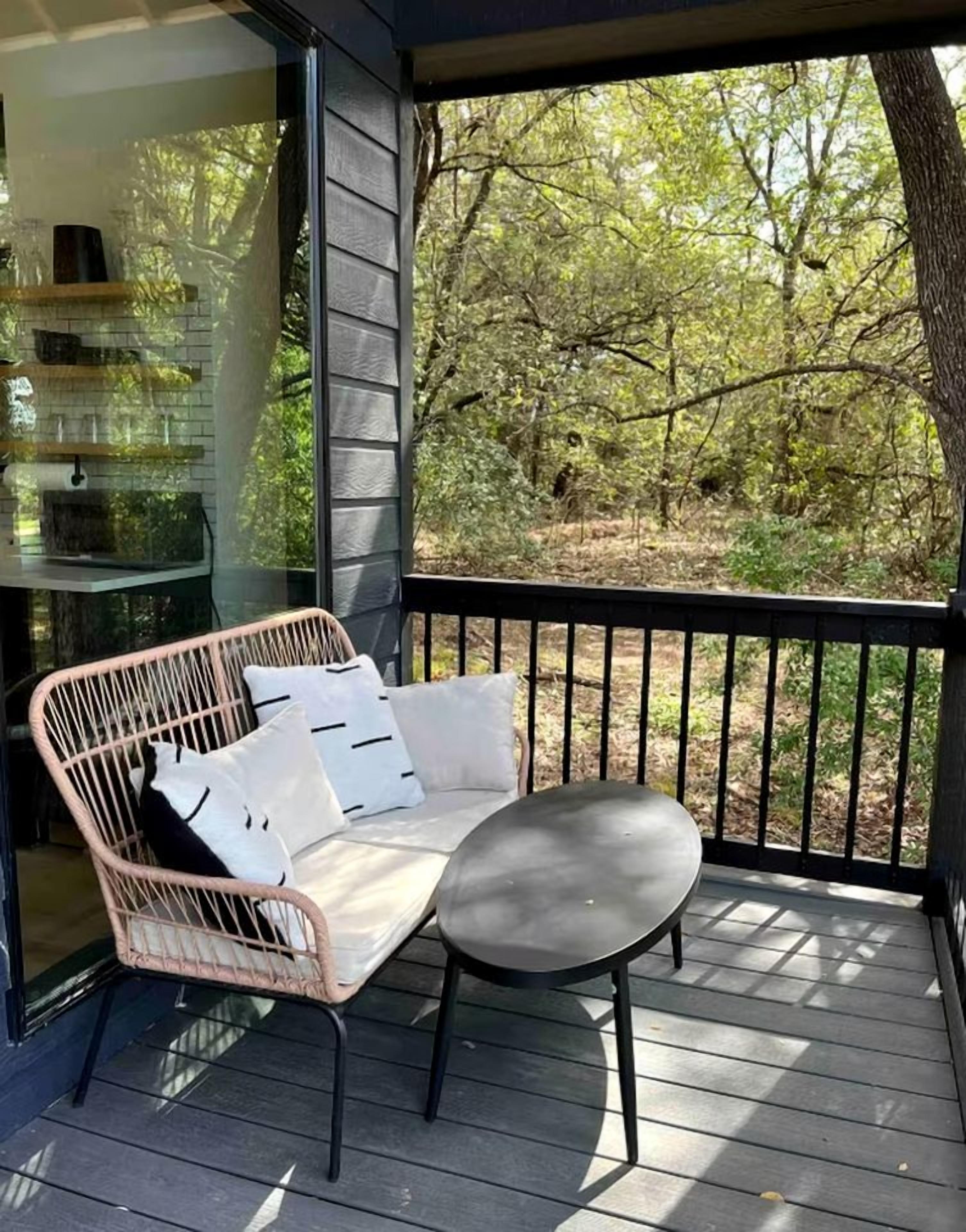 A balcony with a wicker sofa and a small table, overlooking a wooded area.