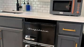 A kitchen with a black refrigerator, a microwave, a sink, and a window with a view of trees.