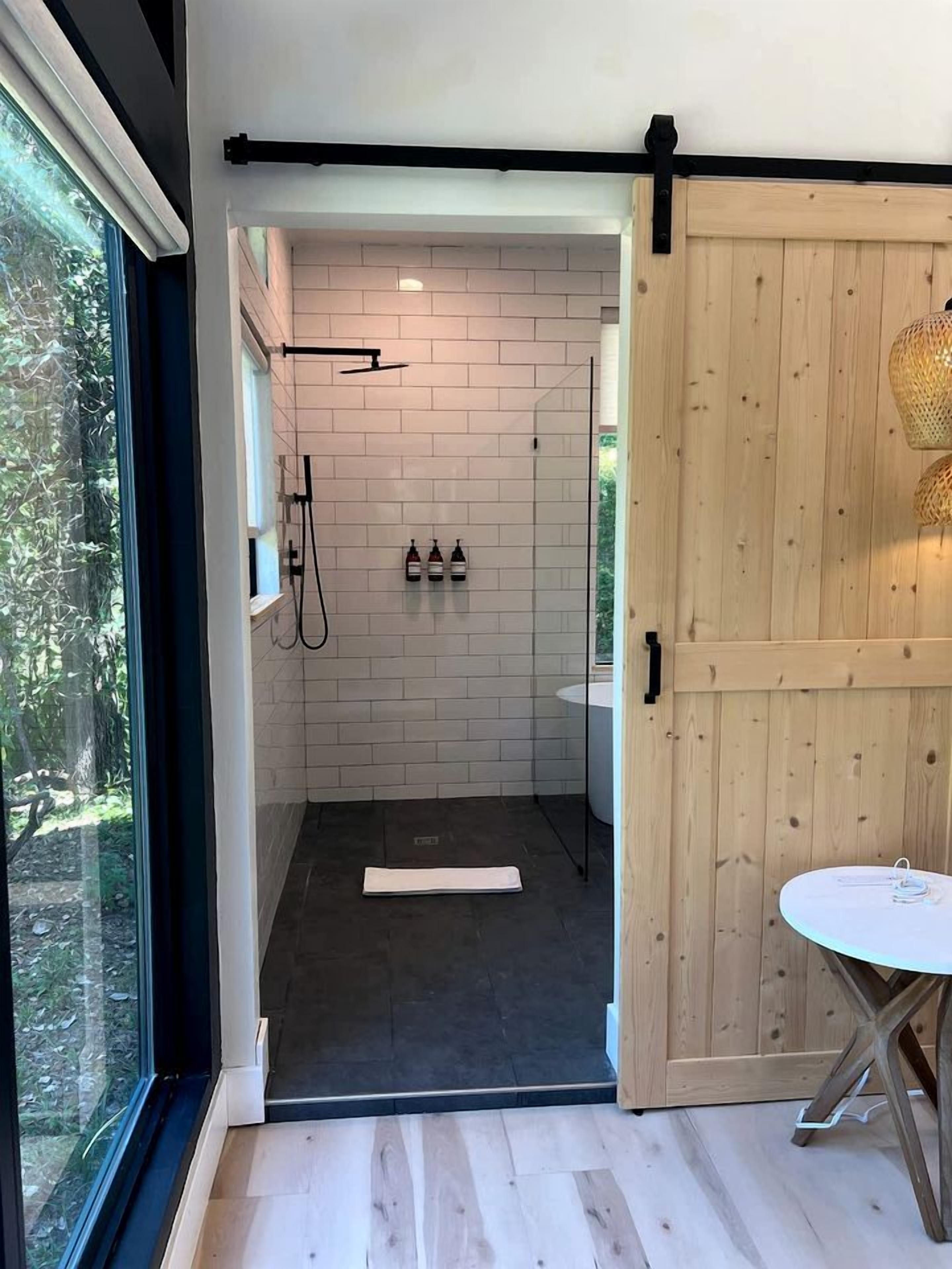 A modern bathroom with a shower, a wooden door, and a view of the outdoors.