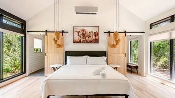 A modern bedroom with a large bed, a painting of cows, and large windows.