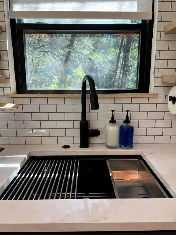 A kitchen with a black faucet, white tiles, and a window with a view of trees.