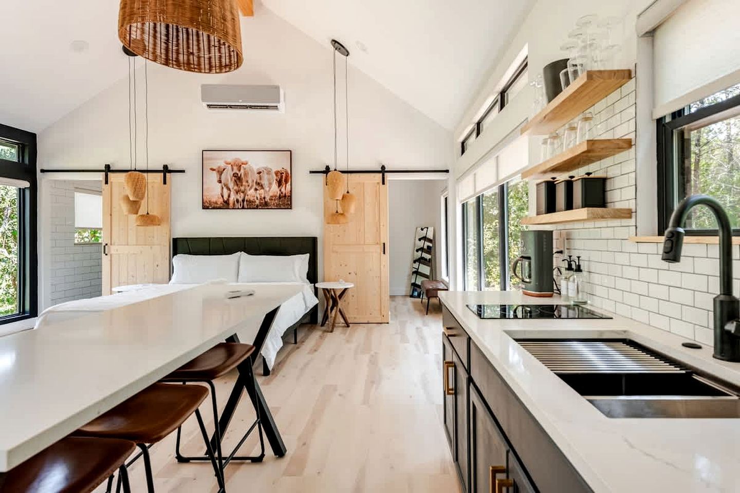 A modern kitchen with a central island, a dining area with a long table and chairs, and a large window providing natural light.