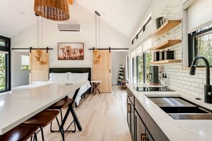 A modern kitchen with a central island, a dining area with a long table and chairs, and a large window providing natural light.