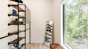 A room with a wooden floor, a black metal rack with shelves, a bench, and a large window with a view of trees.