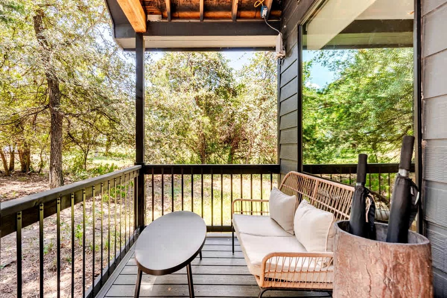 A covered outdoor seating area with a table and a sofa, surrounded by a wooden deck and metal railing.