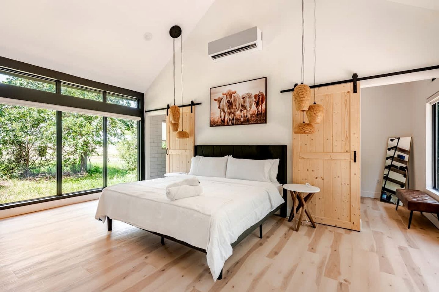Un dormitorio moderno con una cama grande, una mesita redonda pequeña y vistas al verdor exterior.